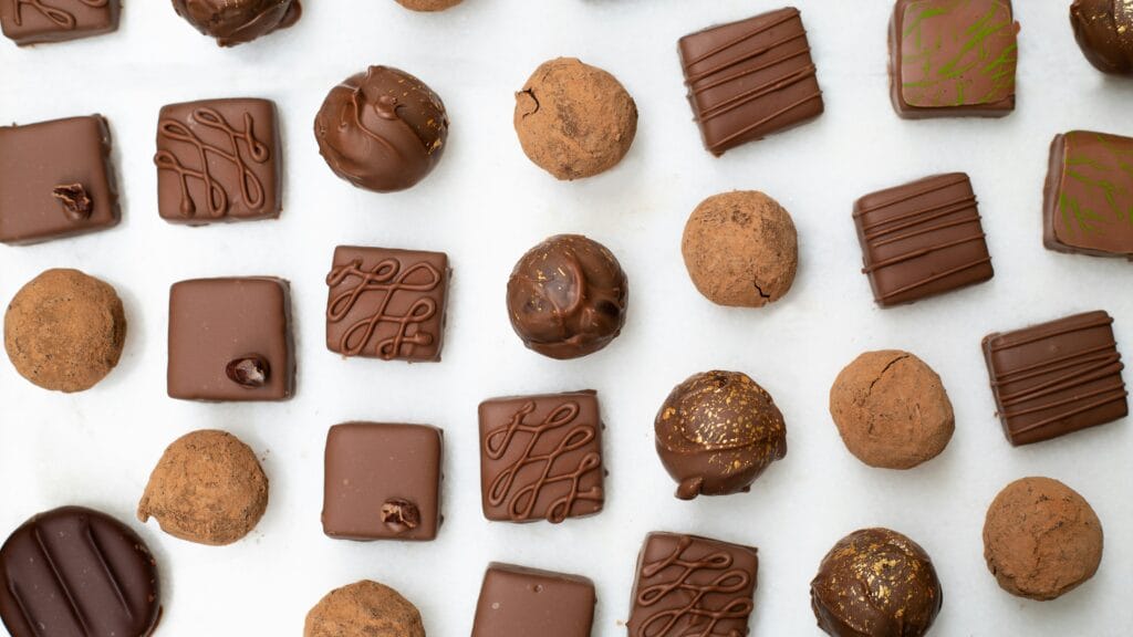 Assorted chocolates and truffles arranged in rows on a light surface.