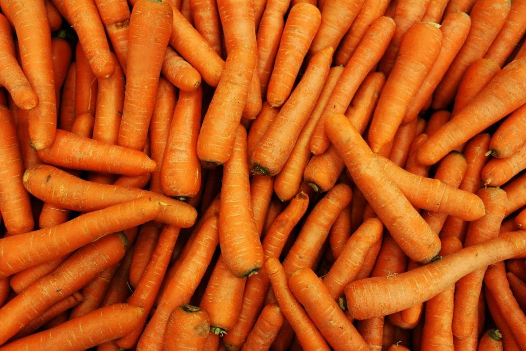 A large pile of whole, unpeeled carrots stacked closely together.