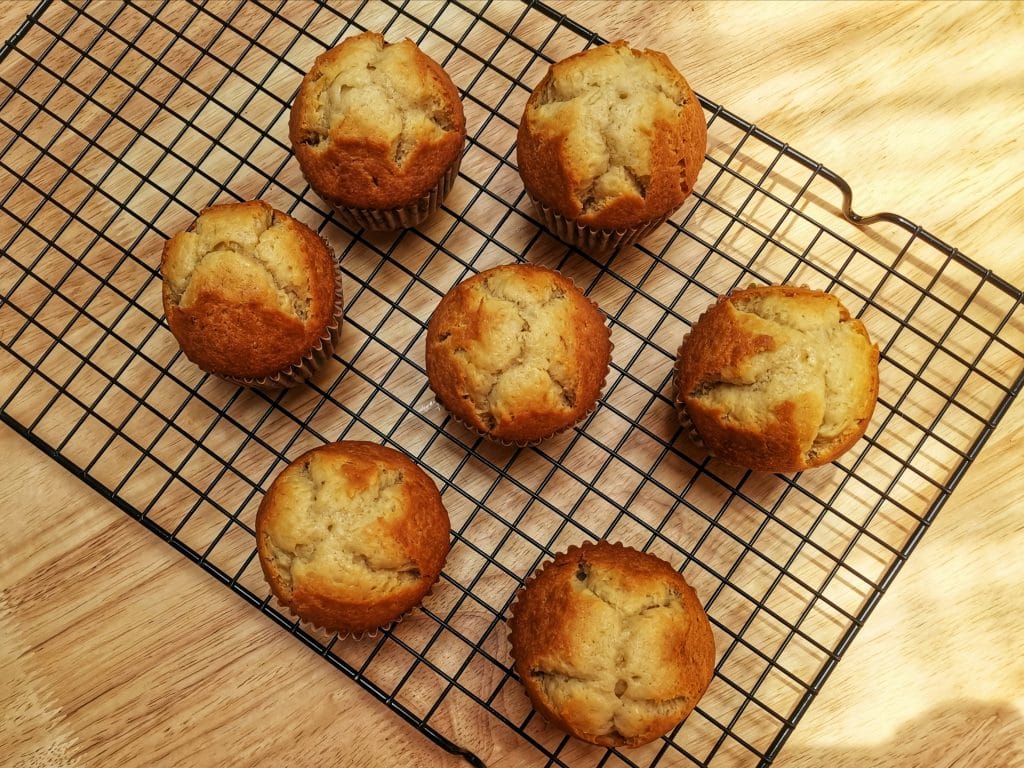Seven muffins cooling on a black wire rack placed on a wooden surface.