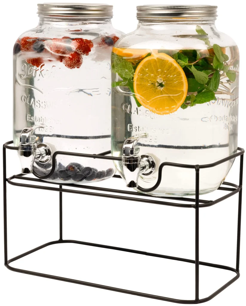 Two glass beverage dispensers with spigots, one filled with water and berries, the other with water, orange slices, and mint, placed on a metal stand.