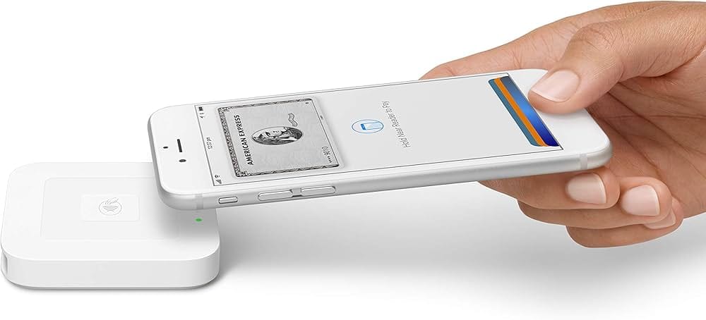 A hand holds an iPhone with Apple Pay open over a white Square card reader, ready to make a contactless payment.