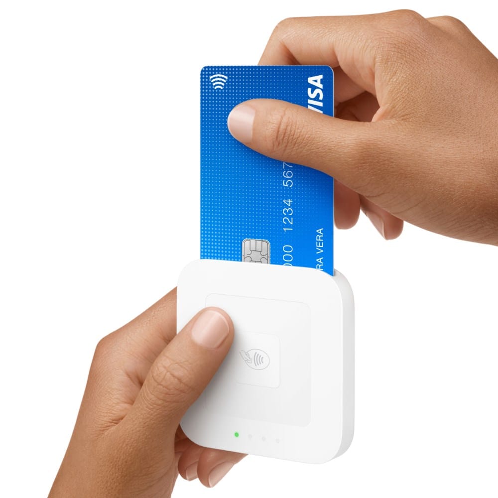 A person inserts a blue Visa credit card into a white card reader held in their other hand.